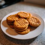 A close-up of several golden brown Easy Peanut Butter Cookies stacked on a white plate, featuring classic fork crosshatch marks.