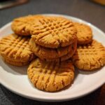A stack of freshly baked Easy Peanut Butter Cookies featuring classic criss-cross fork marks, served on a white plate.