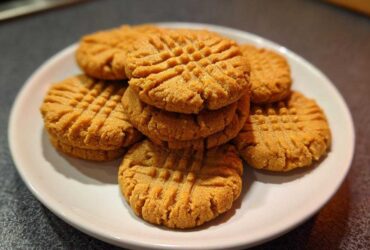 A stack of freshly baked Easy Peanut Butter Cookies featuring classic criss-cross fork marks, served on a white plate.