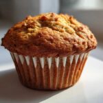 A single, perfectly baked banana protein muffin with a golden brown, domed top, sitting in a white liner.