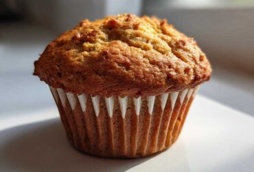 A single, perfectly baked banana protein muffin with a golden brown, domed top, sitting in a white liner.