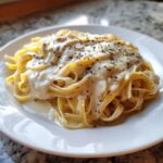 A plate of fettuccine pasta generously coated in creamy Olive Garden Alfredo sauce and sprinkled with herbs.