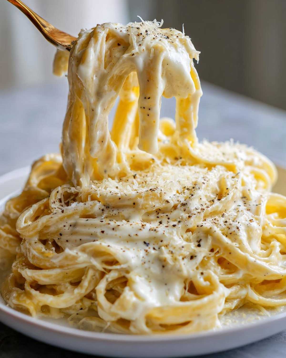 A fork lifting fettuccine noodles coated in rich Olive Garden Alfredo sauce, topped with Parmesan and black pepper.