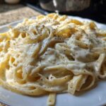 Close-up of fettuccine pasta generously coated in creamy homemade alfredo sauce and topped with cracked black pepper.
