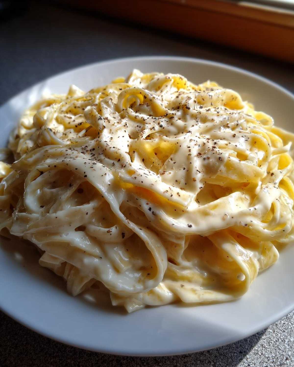 Close-up of fettuccine pasta generously coated in creamy homemade alfredo sauce and sprinkled with black pepper.