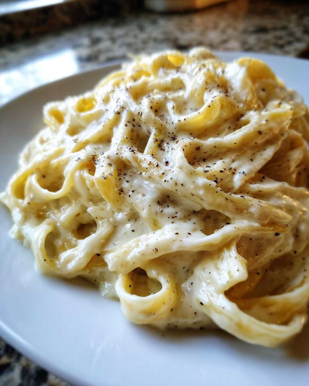Close-up of fettuccine pasta generously coated in rich homemade alfredo sauce and topped with black pepper.