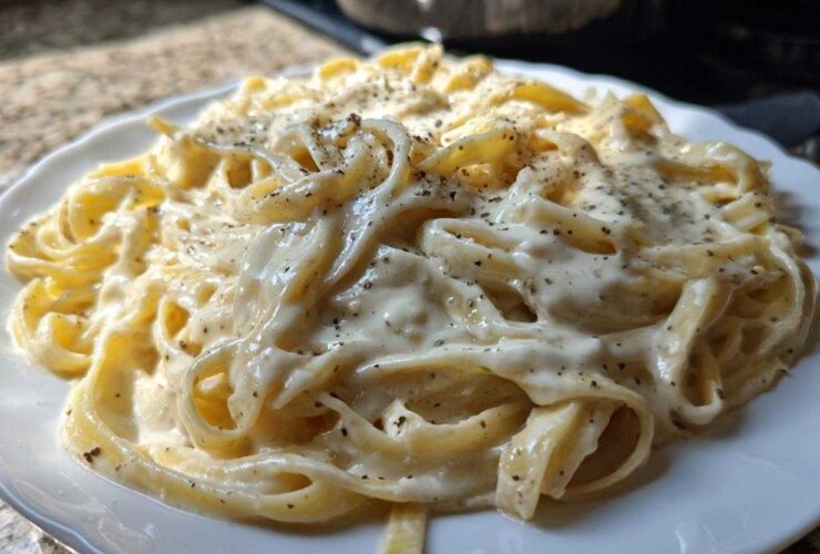 Close-up of fettuccine pasta generously coated in creamy homemade alfredo sauce and topped with cracked black pepper.