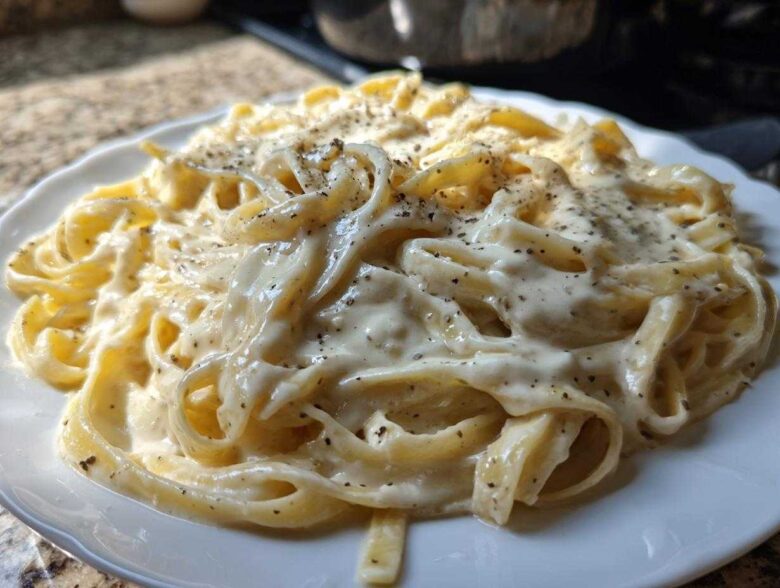 Close-up of fettuccine pasta generously coated in creamy homemade alfredo sauce and topped with cracked black pepper.