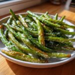 A white bowl filled with roasted, bright green beans sprinkled with coarse salt, ready to eat.