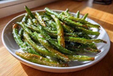 A white bowl filled with roasted, bright green beans sprinkled with coarse salt, ready to eat.