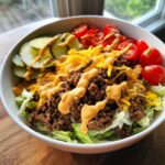 Close-up of a delicious cheeseburger bowl featuring seasoned ground beef, lettuce, pickles, tomatoes, cheese, and special sauce.