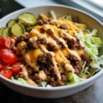 Close-up of a flavorful cheeseburger bowl featuring seasoned ground beef, melted cheddar, special sauce, lettuce, tomatoes, and pickles.