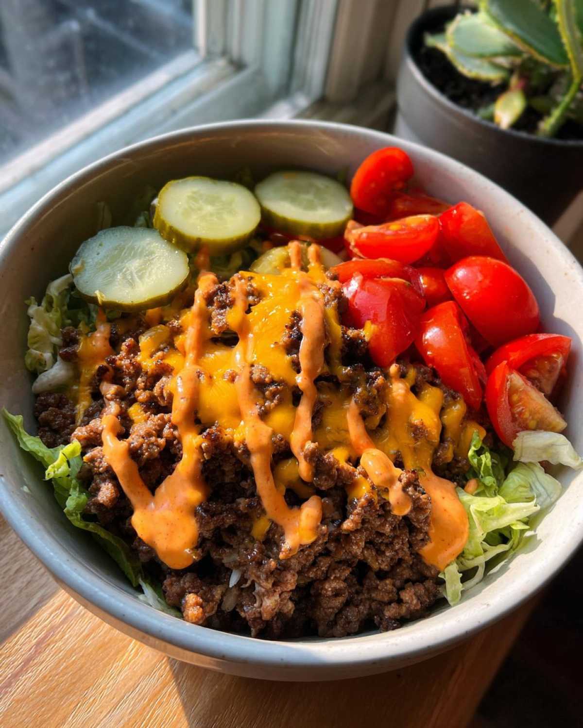 A close-up of a flavorful cheeseburger bowl featuring ground beef, melted cheese, special sauce, pickles, and tomatoes.