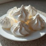 A small pile of perfectly piped, crisp white meringue cookies resting on a white, ridged plate.