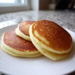 Three perfectly golden brown, fluffy almond flour pancakes stacked on a white plate.