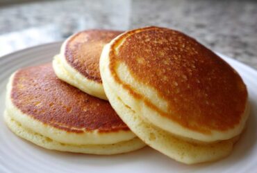 Three perfectly golden brown, fluffy almond flour pancakes stacked on a white plate.