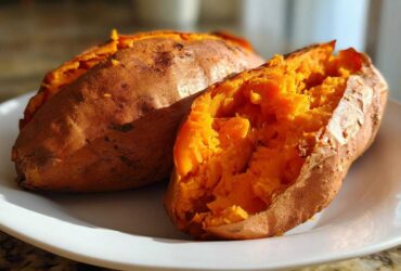 Close-up of a fluffy baked sweet potato split open, revealing bright orange flesh on a white plate.