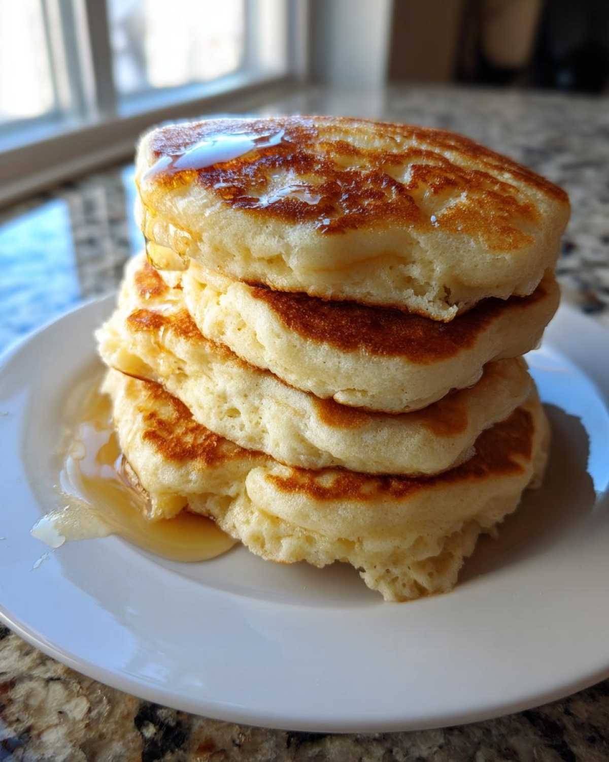 A tall stack of four fluffy greek yogurt pancakes drizzled with maple syrup on a white plate.