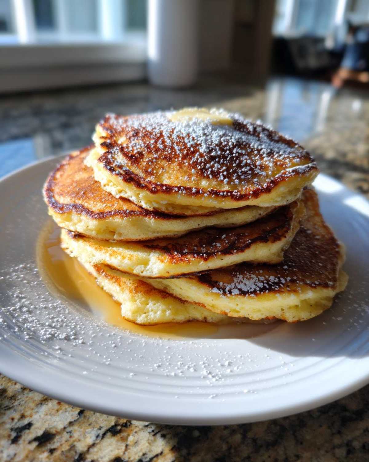 A tall stack of fluffy sourdough pancakes dusted with powdered sugar and drizzled with syrup on a white plate.