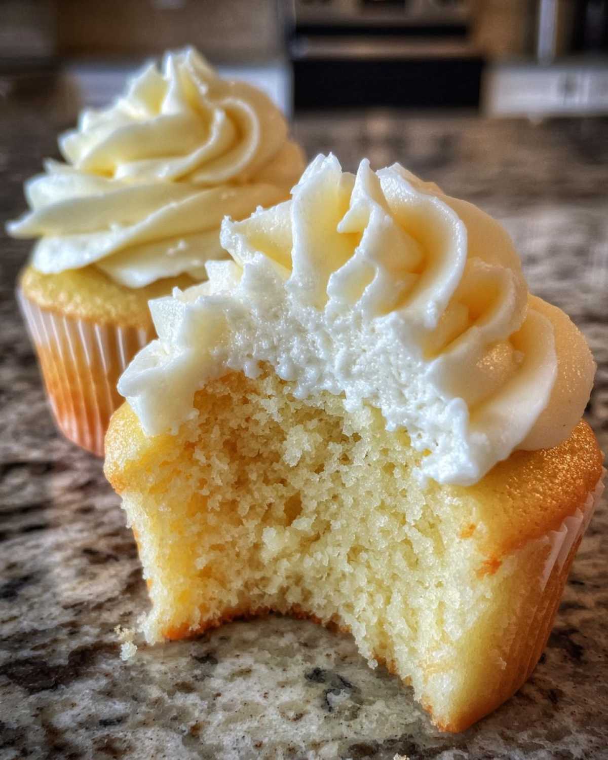 A close-up shot showing a bite taken out of a fluffy vanilla cupcake with rich vanilla frosting.