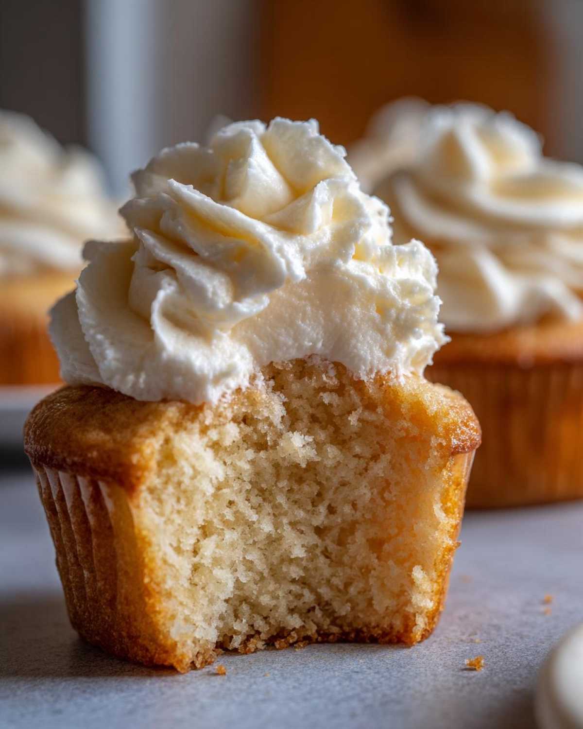Close-up of a vanilla cupcake with a bite taken out, showing the fluffy, moist crumb and rich vanilla frosting.