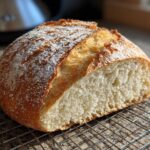 A freshly baked, round loaf of French bread, cut to show the soft interior, resting on a wire cooling rack.