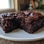 Close-up of two fudgy black bean brownies squares topped with melted chocolate chips on a white plate.