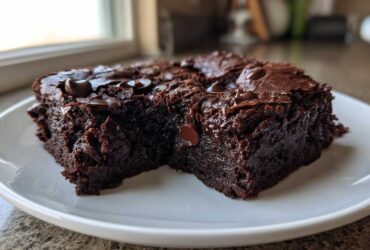 Close-up of two fudgy black bean brownies squares topped with melted chocolate chips on a white plate.