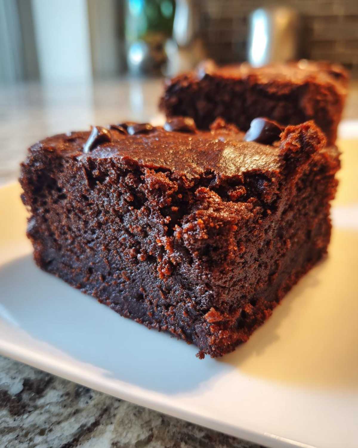 A close-up, rich, dark chocolate square of fudgy sweet potato brownies resting on a white plate.
