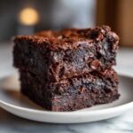 Two stacked, rich, dark chocolate sweet potato brownies with visible chocolate chips on a white plate.