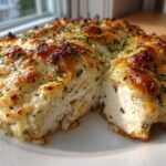 A thick slice of juicy Garlic parmesan chicken bake showing moist white chicken topped with a bubbly, golden-brown cheese crust and parsley.