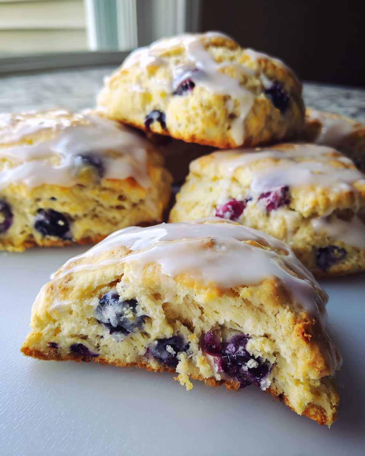 A close-up shot showing a stack of glazed blueberry scones, with one cut open revealing the moist interior and plump blueberries.