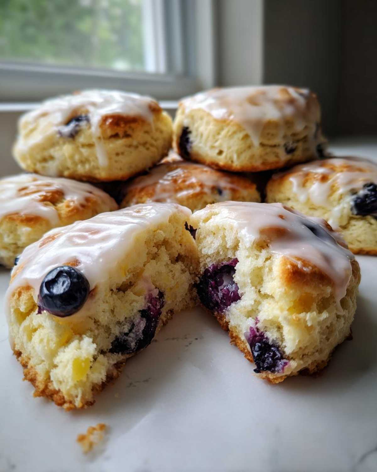 A stack of freshly baked blueberry scones topped with a white glaze, one scone is broken open showing the interior.