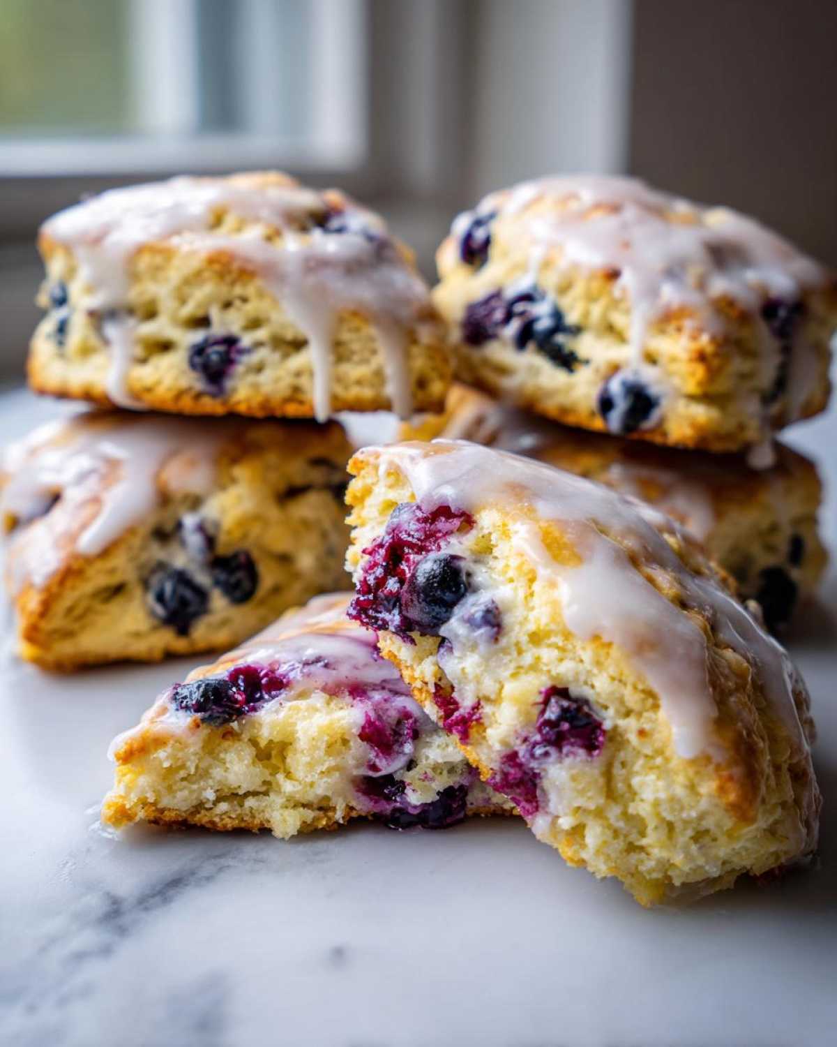A stack of glazed blueberry scones with one cut in half showing the moist interior packed with berries.