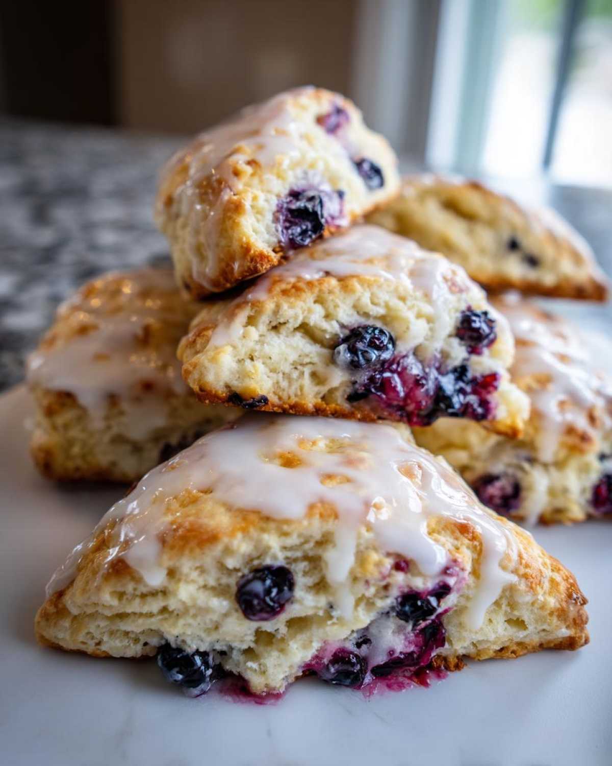 A close-up stack of freshly baked blueberry scones topped with a sweet white glaze, featuring juicy, burst blueberries.