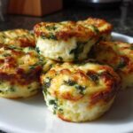 A stack of five golden brown, baked egg bites mixed with spinach, served on a white plate.