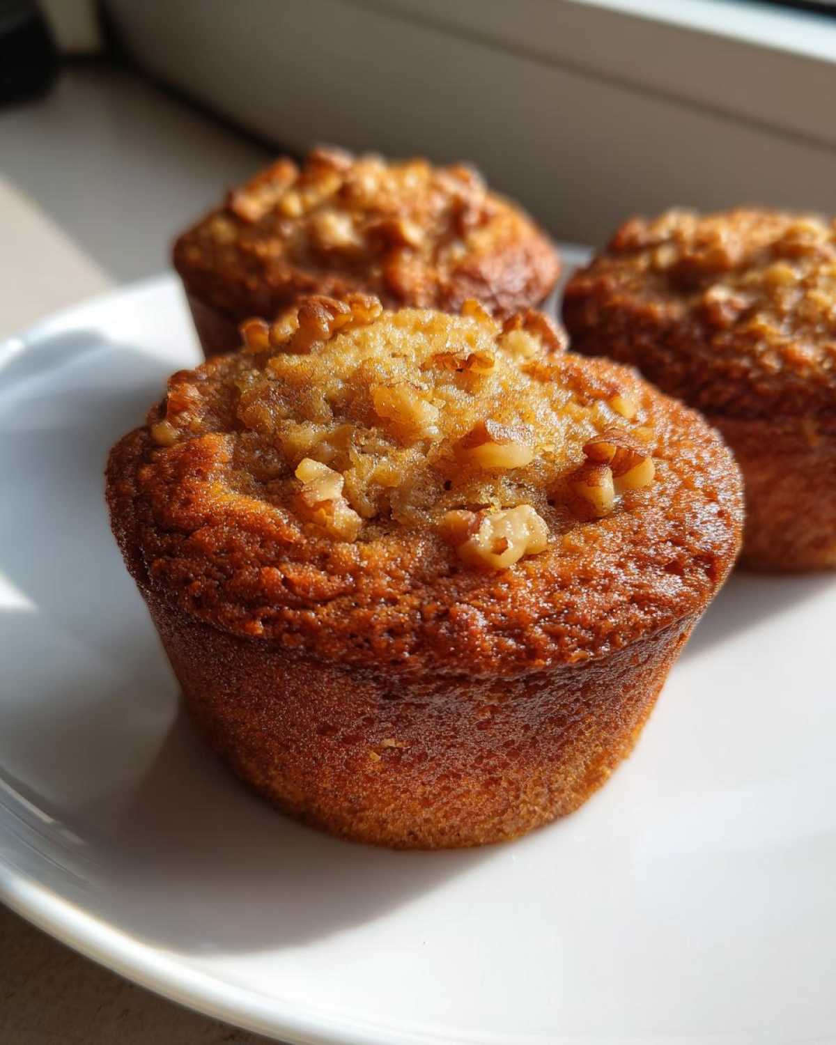 Close-up of three golden brown banana nut muffins topped with walnuts resting on a white plate.