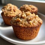 Close-up of freshly baked banana nut muffins topped with crunchy walnuts on a white plate.