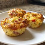 Three golden brown Egg Muffin Cups filled with ham and peppers served on a white plate.