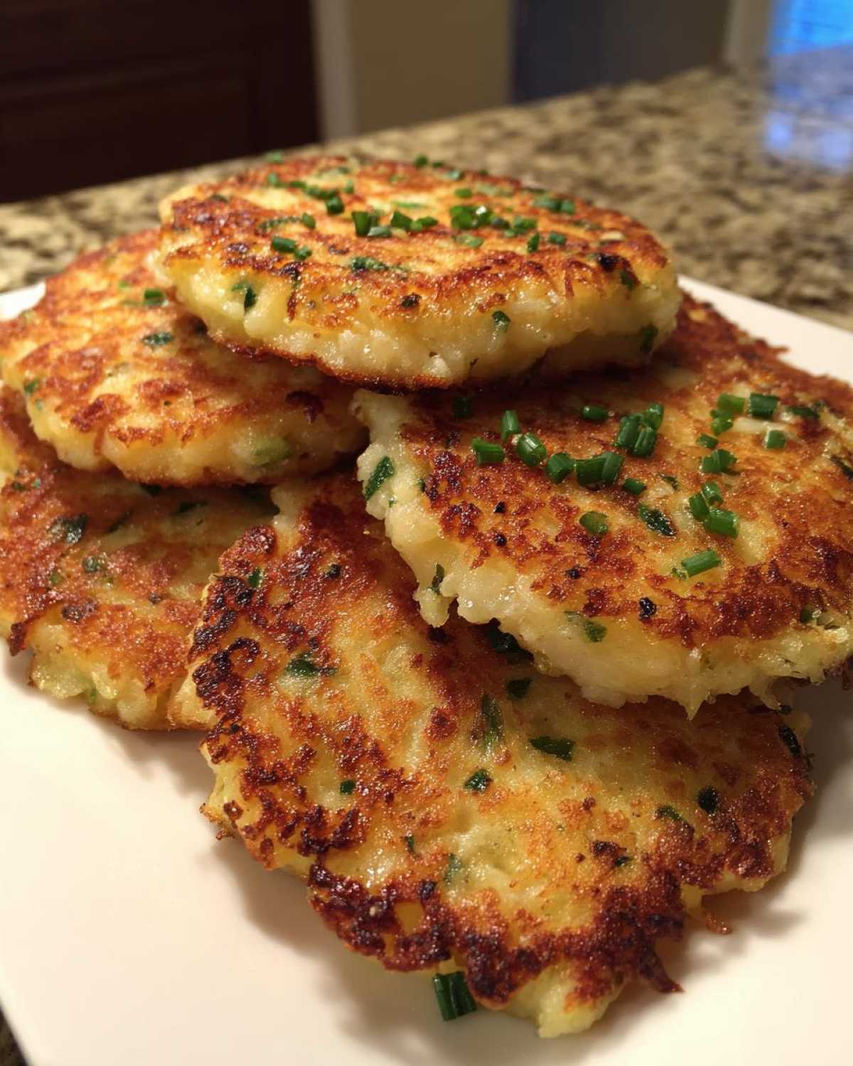 A stack of golden brown, pan-fried mashed potato cakes garnished with freshly chopped chives.