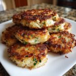 A stack of golden brown, pan-fried mashed potato cakes flecked with green herbs on a white plate.