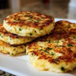 A stack of perfectly pan-fried mashed potato cakes, golden brown with visible green herbs.