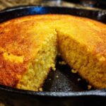 Close-up of golden brown skillet cornbread with a piece cut out, showing the crumb texture.