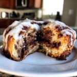 A gooey, freshly baked cinnamon roll cut in half, showing the rich cinnamon swirl filling and thick white icing.