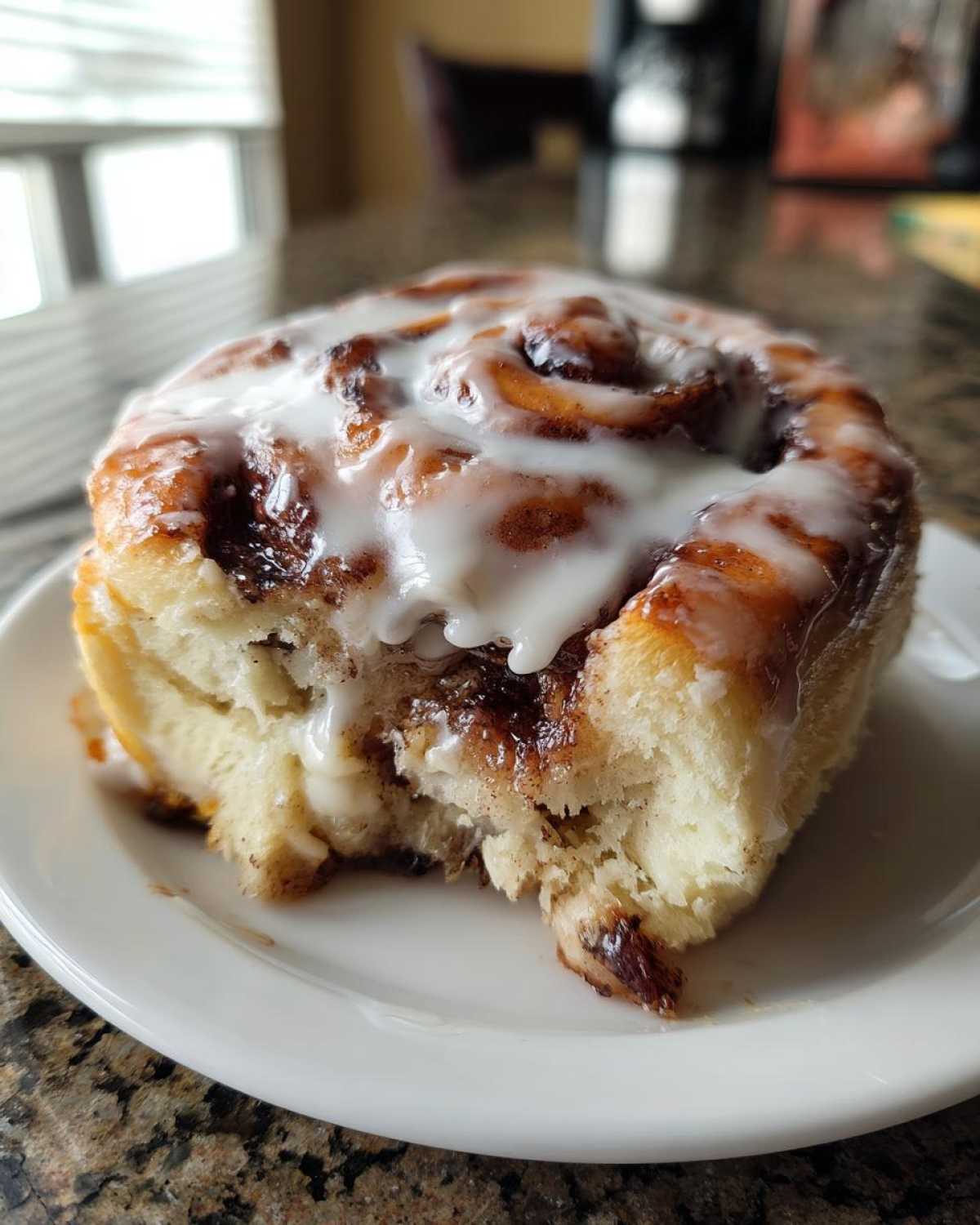 A close-up photo of a soft, gooey cinnamon roll topped with white icing, with a bite taken out.
