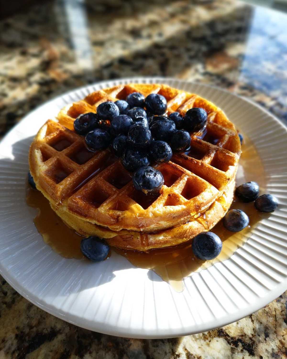 A stack of golden brown high protein waffles topped with fresh blueberries and drizzled with syrup.