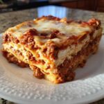 A generous slice of layered lasagna with cottage cheese filling, meat sauce, and melted cheese topping.