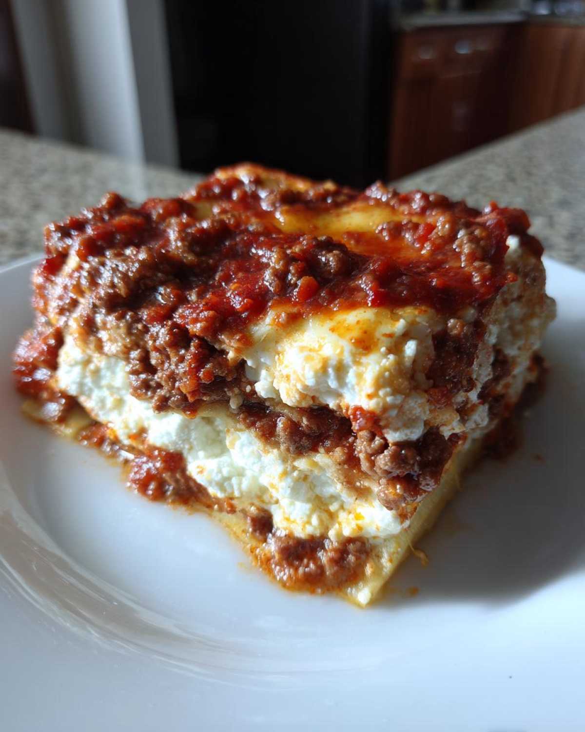 A close-up of a hearty slice of lasagna with cottage cheese, layered with meat sauce, served on a white plate.