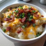 Close-up of a white bowl filled with chunky loaded baked potato soup, topped with melted cheddar cheese, bacon bits, and green onions.