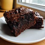 Two rich, dark slices of moist black bean brownies topped with melted chocolate chips on a white plate.